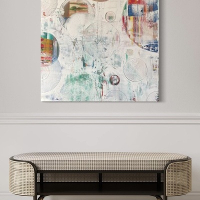 Quadro abstrato de círculos coloridos numa parede branca sobre banco estofado com vime