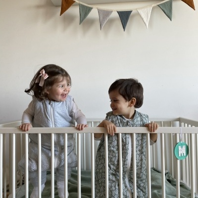 Crianças em cama de bebé branca com decoração de bandeirolas e quadros com animais na parede