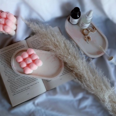 velas cor de rosa em forma de cubos de bolhas sobre base rosa, com folhas secas, livro aberto e bandeja com frascos e joias