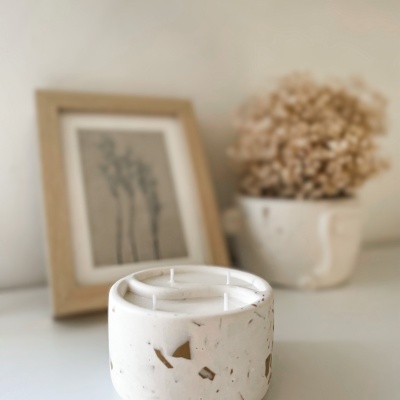 Vela branca com recipiente marmoreado e fundo com quadro e flores secas