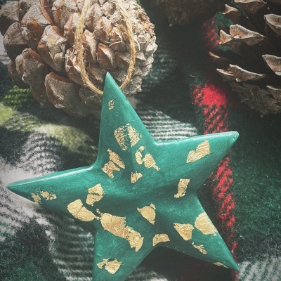 Estrela decorativa verde com detalhes dourados sobre tecido xadrez e pinhões naturais