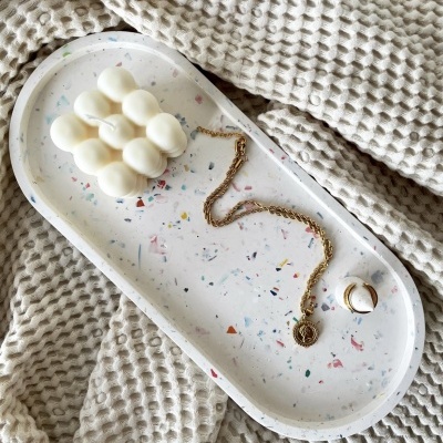 Tabuleiro oval com vela, corrente dourada e anel sobre tecido bege texturizado