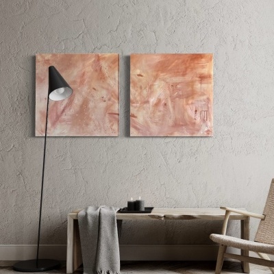 Duas pinturas abstratas rosas penduradas em parede cinzenta com lâmpada de pé, banco de madeira com manta e velas, e cadeira de madeira.