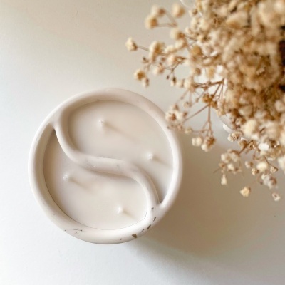 Vela branca em recipiente cerâmico com design em 'S' e flores secas ao lado