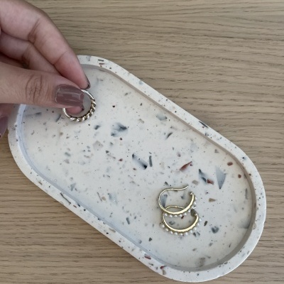 Brincos dourados com pequenas pérolas numa bandeja de terrazzo sobre mesa de madeira clara