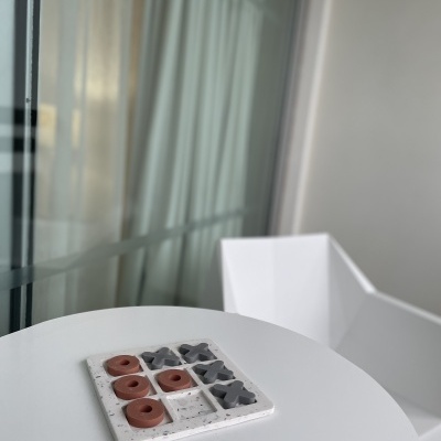 Jogo da velha com peças castanhas e pretas sobre mesa branca com cadeira branca ao lado