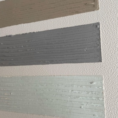 Amostras de tinta em tons castanho, cinzento e verde claro aplicadas em papel texturizado