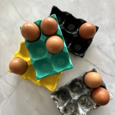 Quatro caixas coloridas para ovos com ovos castanhos em cima de uma superfície branca marmorizada