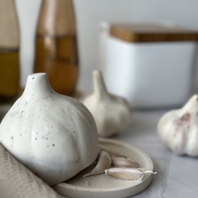 Alhos inteiros e dentes de alho num prato branco com recipiente e garrafas ao fundo