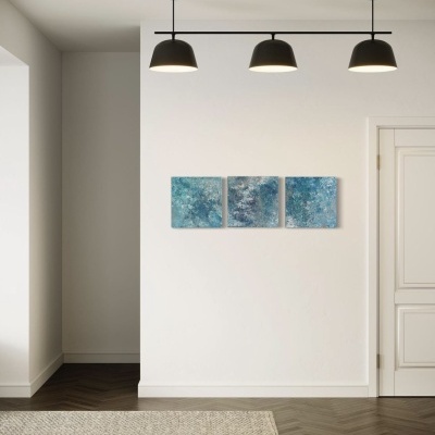 Três quadros abstratos em tons de azul pendurados numa parede branca sob três candeeiros pretos num espaço interior moderno