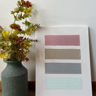 Tela branca com faixas horizontais coloridas em relevo ao lado de um vaso verde com folhas artificiais