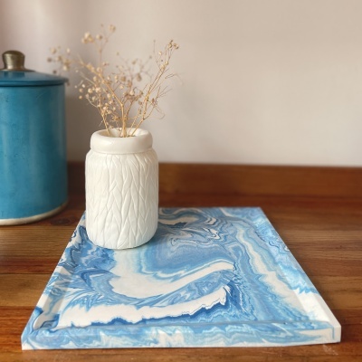 Vaso cerâmico branco com textura e flores secas em placa marmorizada azul sobre mesa de madeira