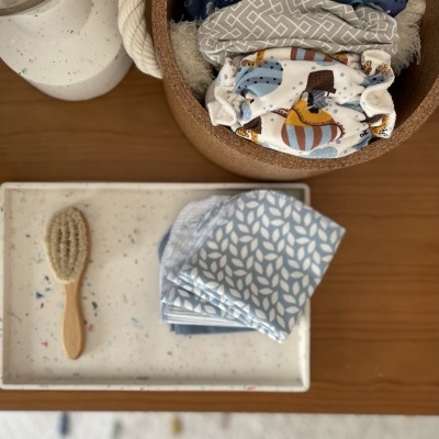 Fraldas reutilizáveis coloridas em recipiente redondo com escova e tecido azul claro em bandeja branca