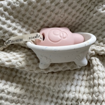 Sabonete rosa em forma de animal numa banheira branca sobre tecido bege texturizado