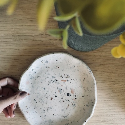 Prato cerâmica branca salpicada com bordas onduladas e vaso com flores amarelas sobre mesa de madeira