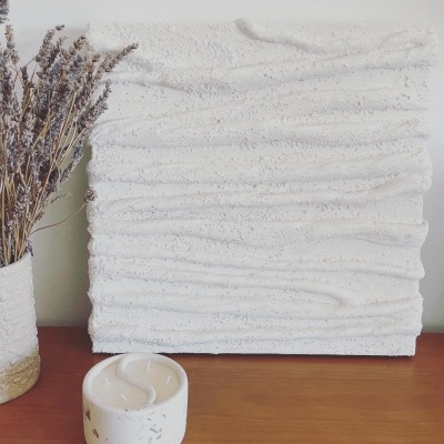 Escultura white texturizada com vaso de cerâmica e vela em cima de superfície de madeira.