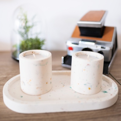 Duas velas brancas com manchas coloridas numa bandeja branca sobre mesa de madeira