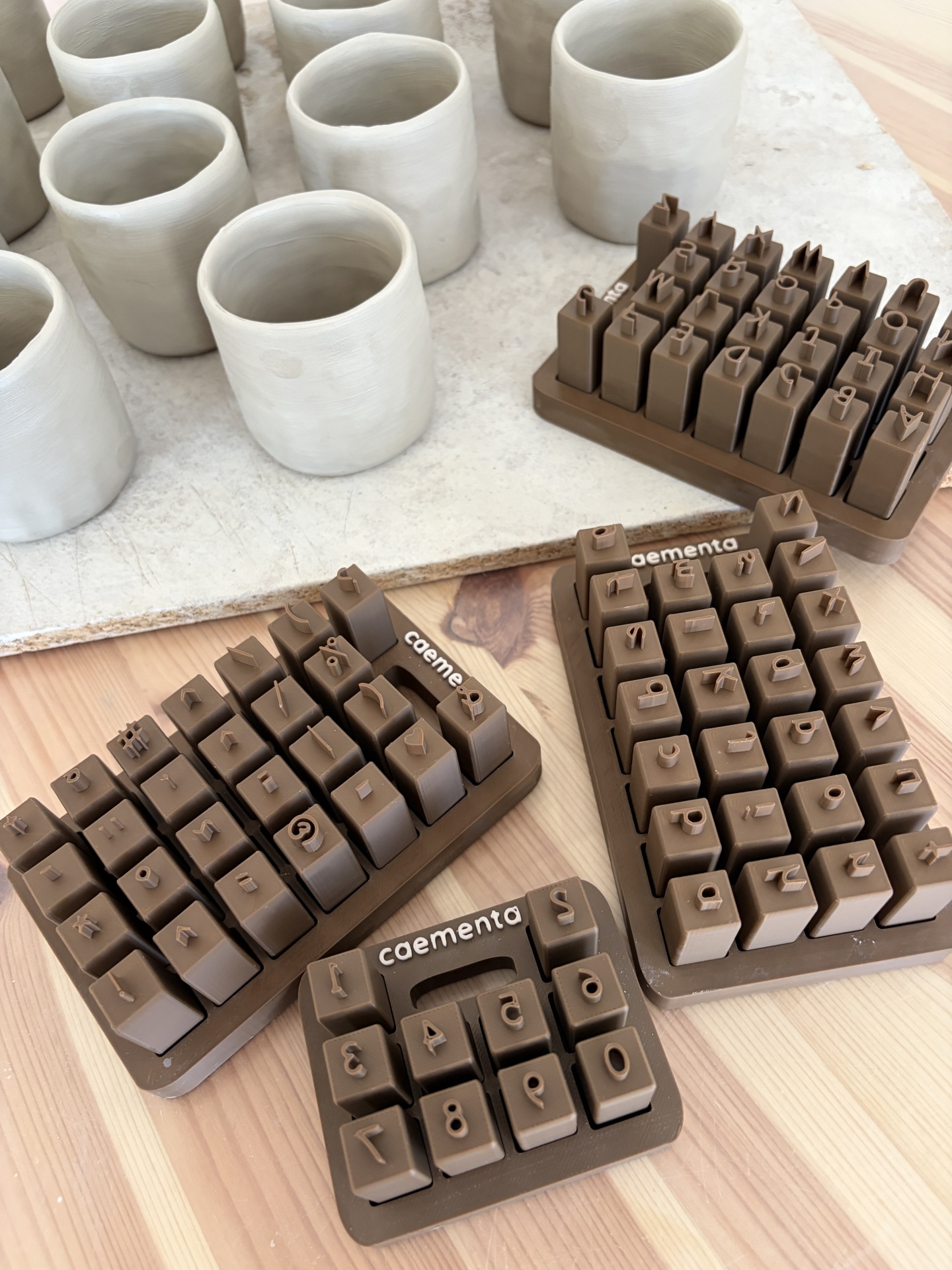 Conjunto de carimbos de letras e números em plástico castanho com copos de cerâmica brancos sobre mesa de madeira.