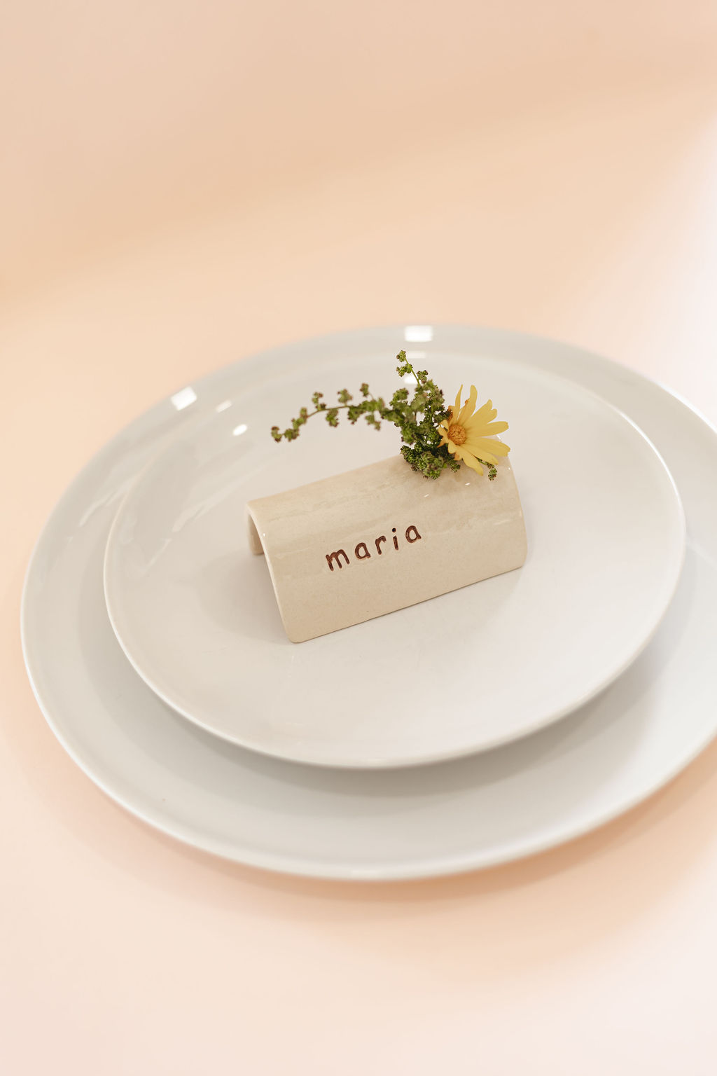 Marcador de mesa em cerâmica com nome Maria e flor sobre pratos brancos