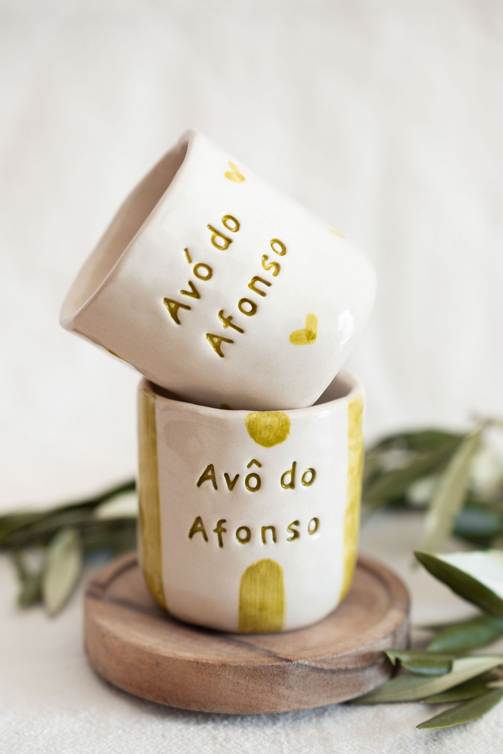 Dois copos de cerâmica brancos com texto gravado Avô do Afonso e detalhes amarelos sobre base de madeira
