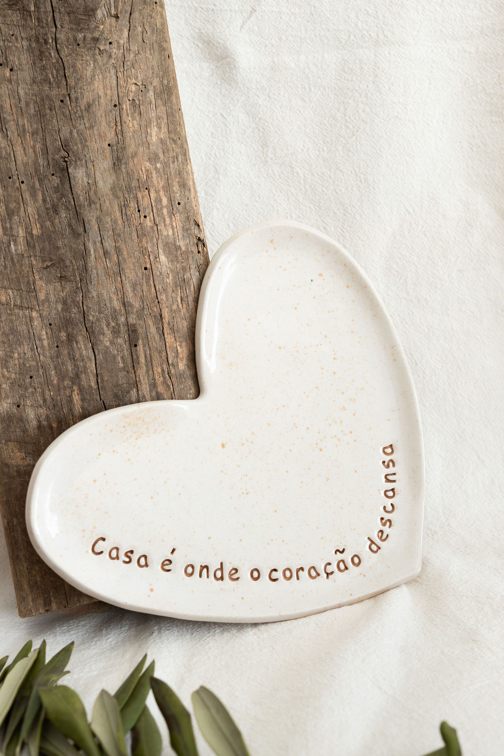 Prato cerâmico em forma de coração com frase em português sobre madeira e tecido branco