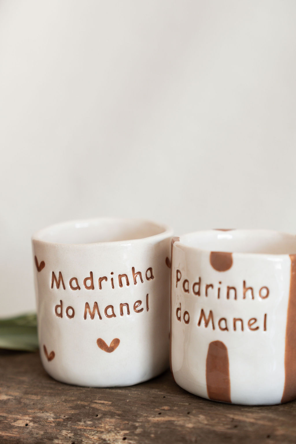 Conjunto de duas canecas cerâmicas brancas com texto e padrões castanhos sobre uma superfície de madeira