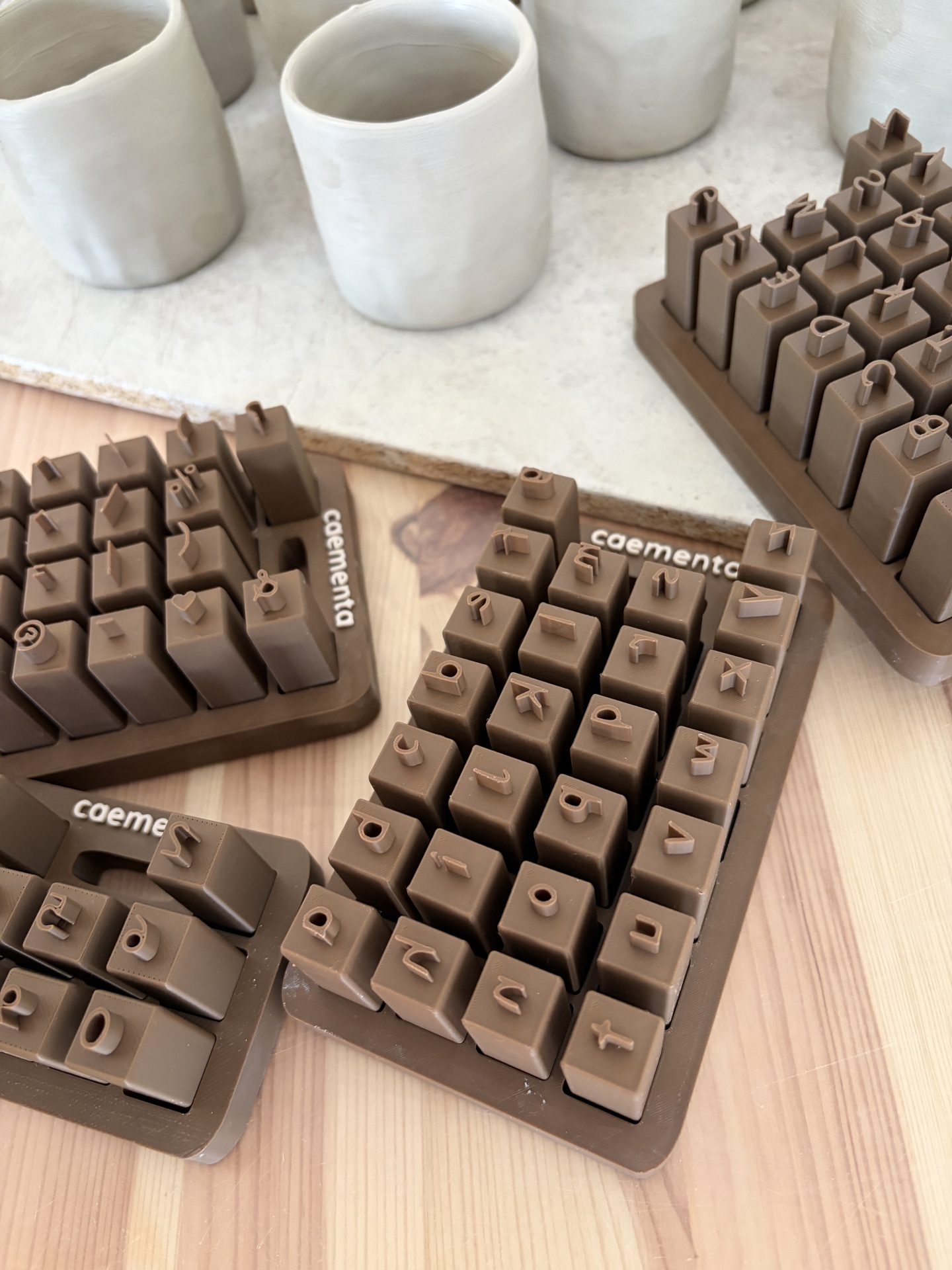 Conjuntos de carimbos em silicone castanho com letras e números, base caementa, mesa de madeira, vasos cinza claro
