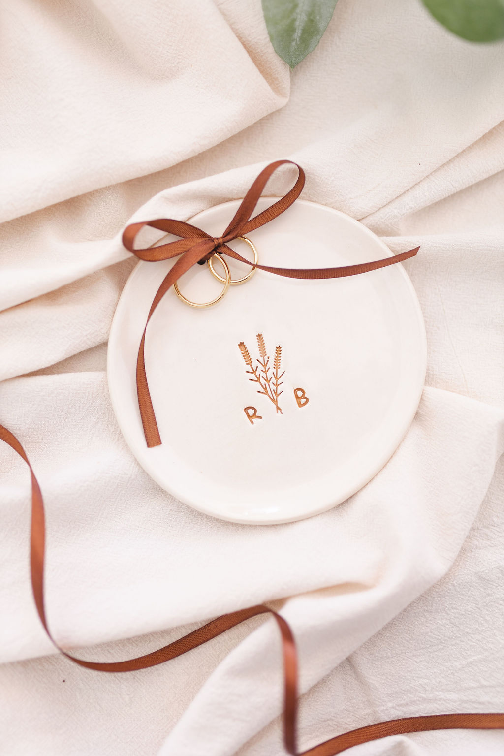 Prato branco em cerâmica com gravura dourada e alianças amarradas com fita castanha