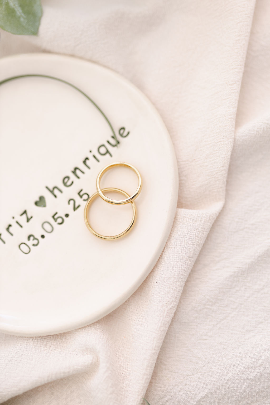 Anel dourado sobre um prato branco com texto e decoração verde sobre tecido branco.