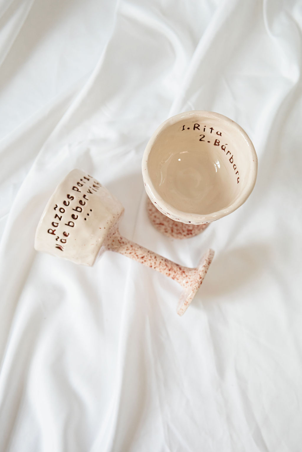 Dois copos de cerâmica rosa com frases escritas em castanho sobre fundo branco.