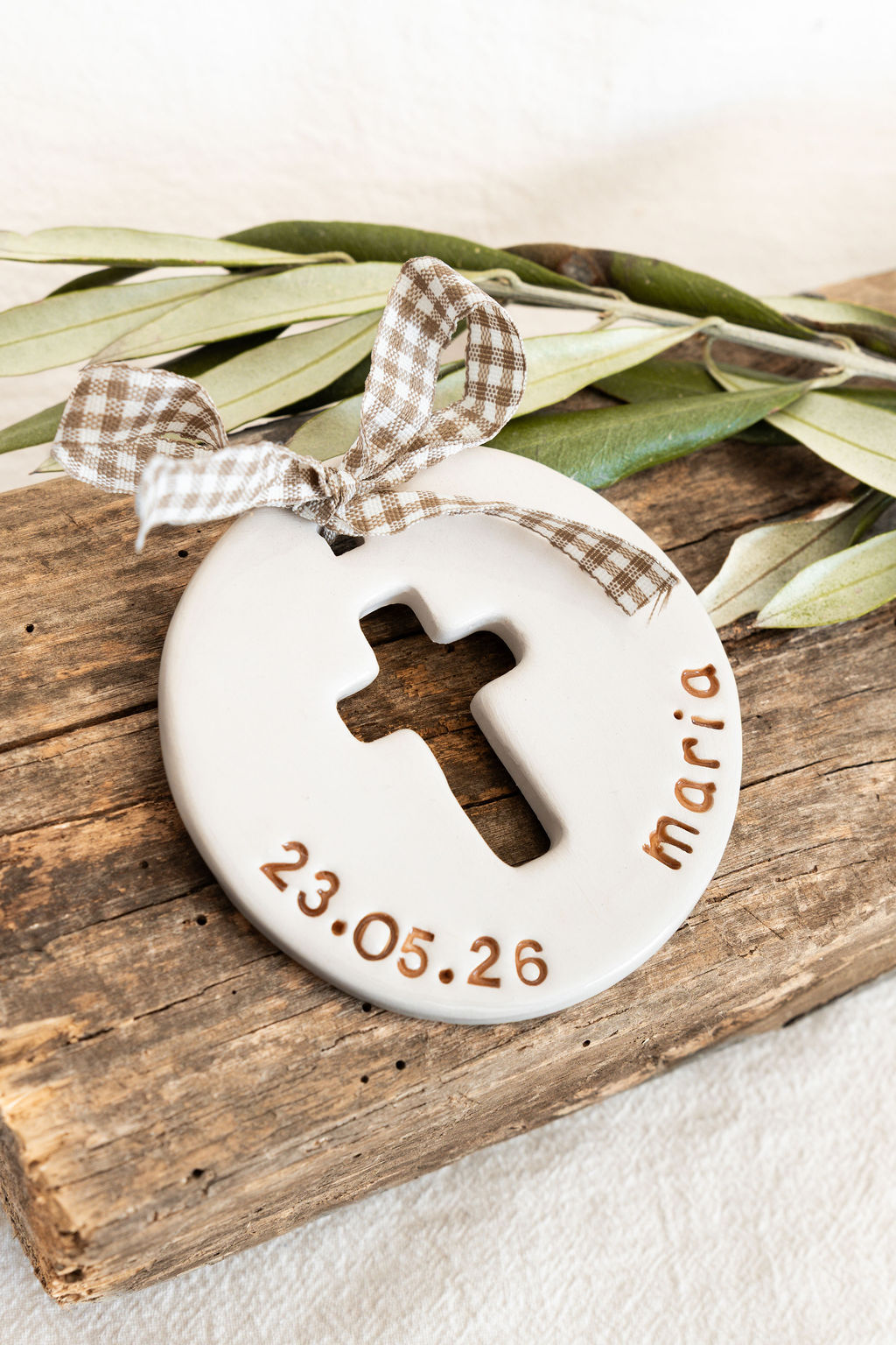 Ornamento redondo branco com cruz recortada, fita xadrez e inscrições sobre madeira