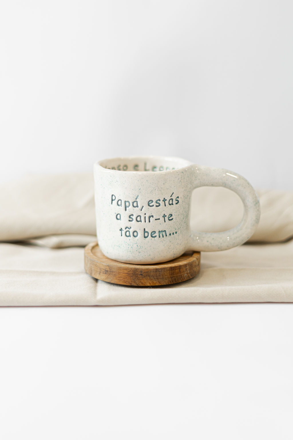 Caneca branca com texto em português sobre base de madeira