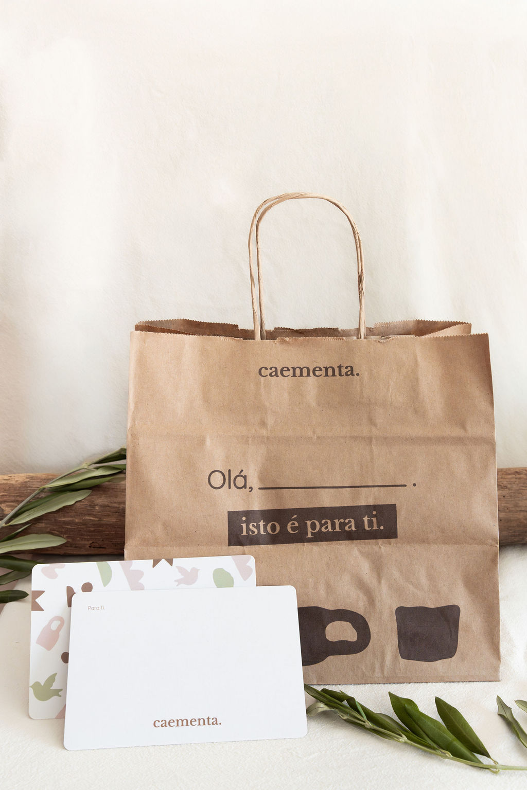 Saco de papel castanho para transporte com texto impresso e dois cartões brancos com folhas verdes