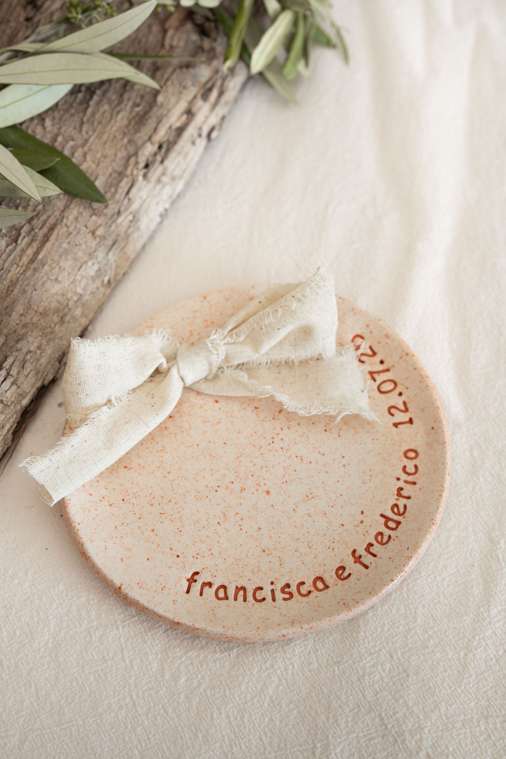 Prato redondo bege com manchas castanhas, fita de tecido amarrada e texto decorativo ao redor