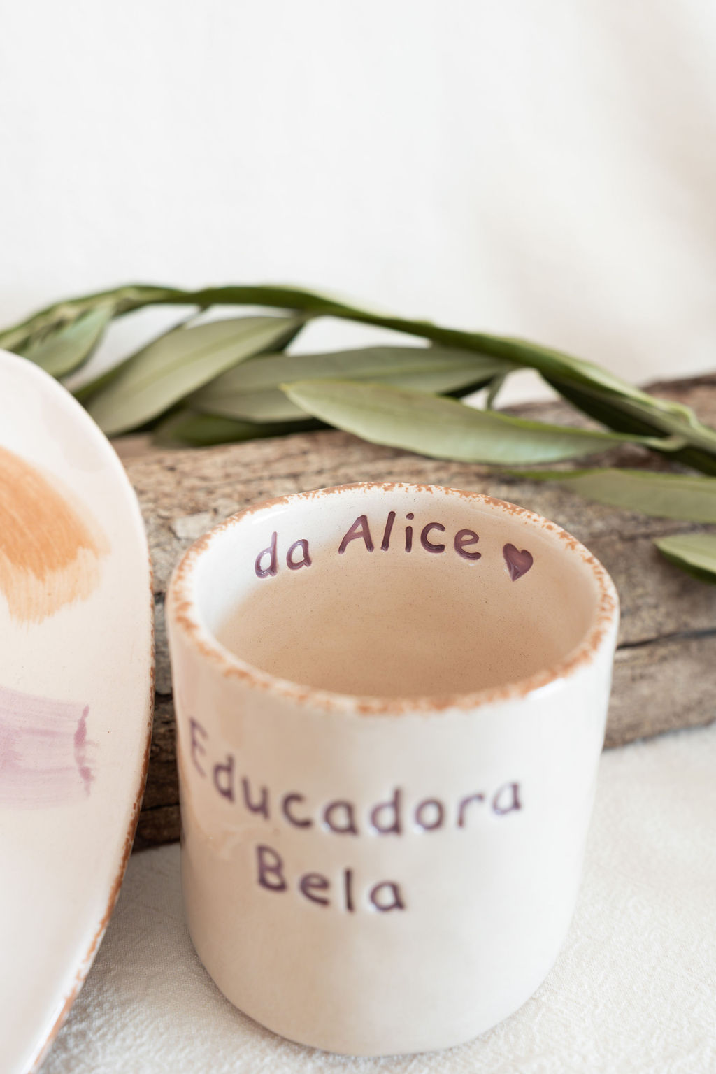 Caneca de cerâmica branca com texto e prato ao lado sobre tecido branco