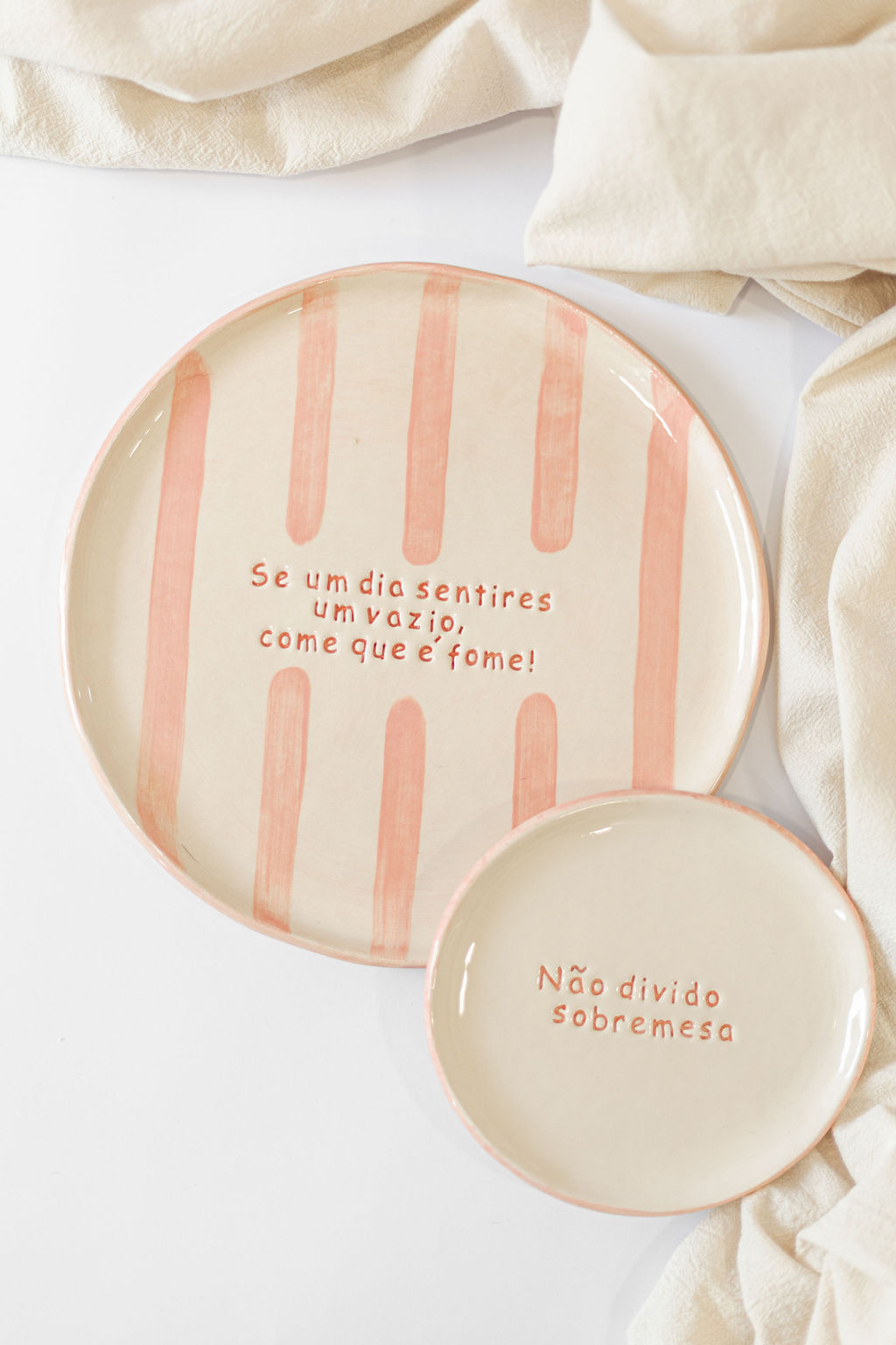 Dois pratos cerâmica bege e rosa com texto em português sobre fundo branco e tecido bege