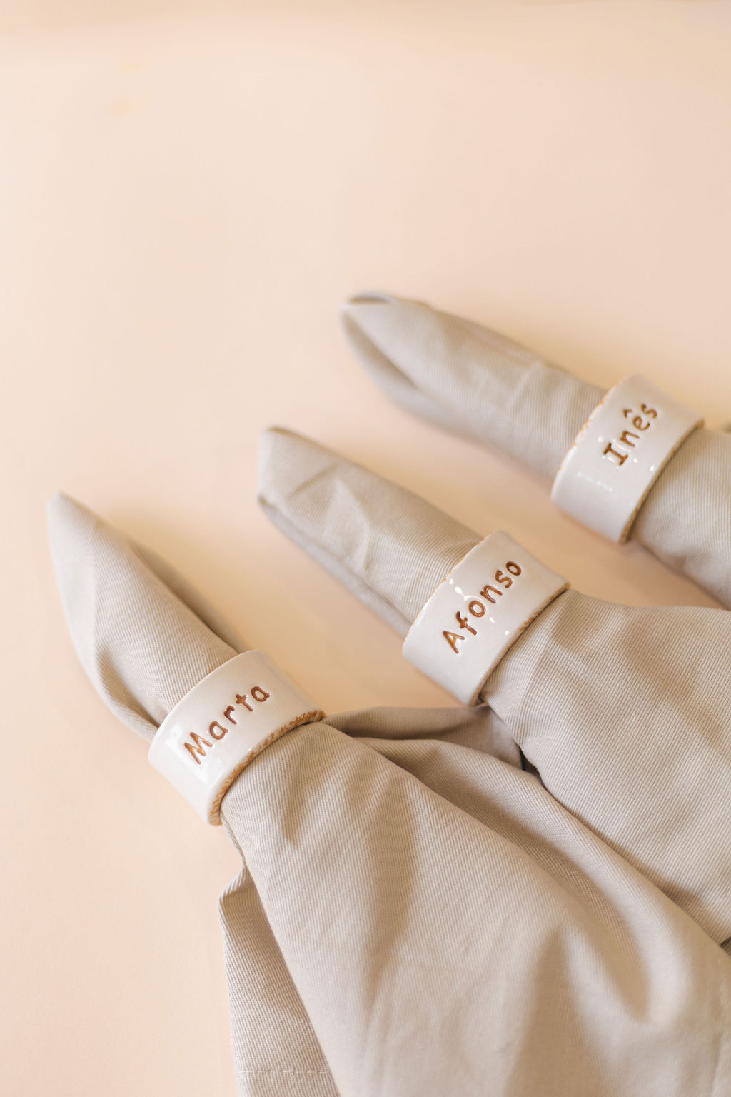Guardanapos de tecido bege com anéis de cerâmica branca personalizados com nomes Marta, Afonso e Inês