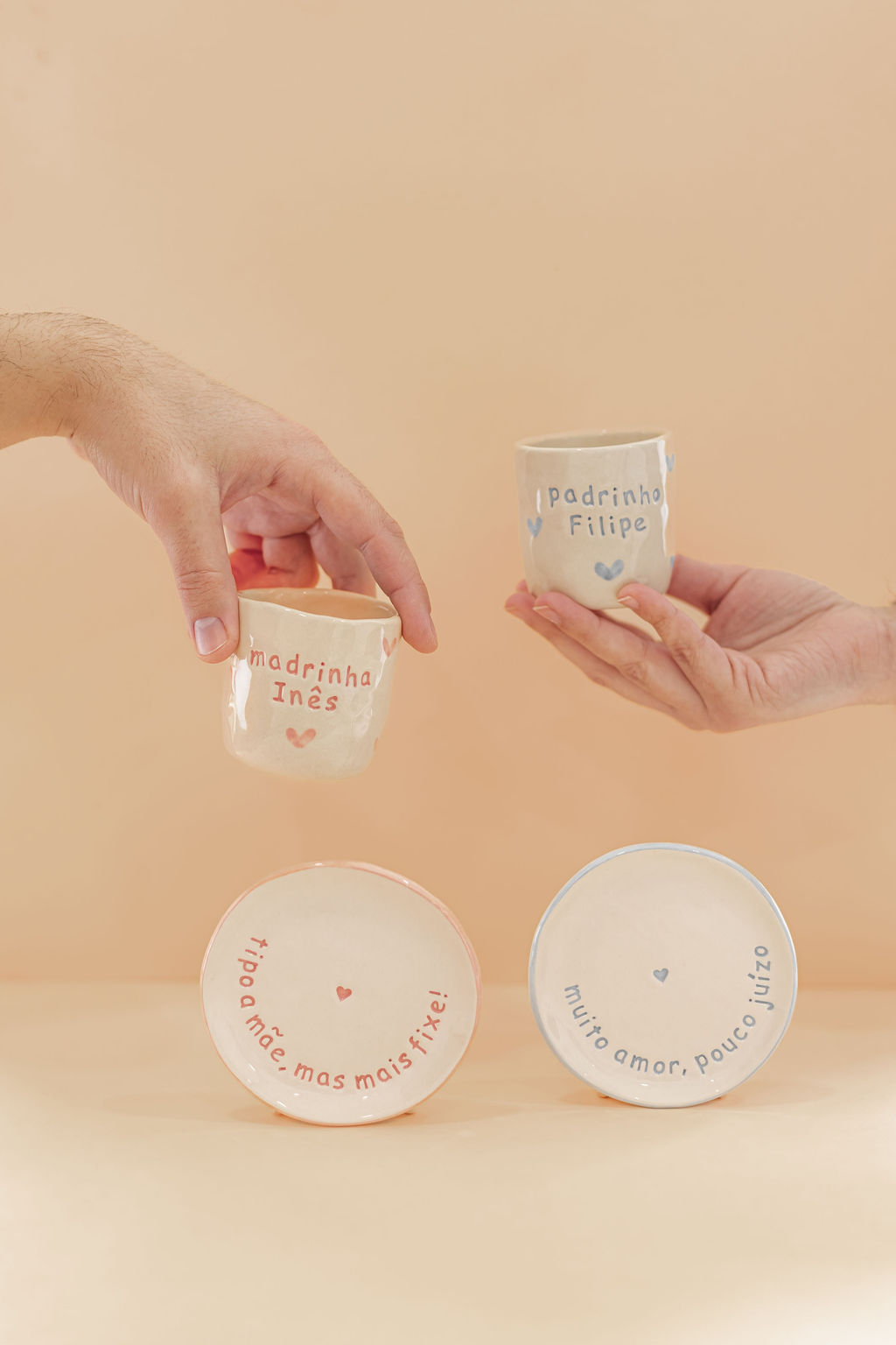Conjunto de peças cerâmicas personalizadas, duas canecas e dois pratos com textos em português e corações decorativos.