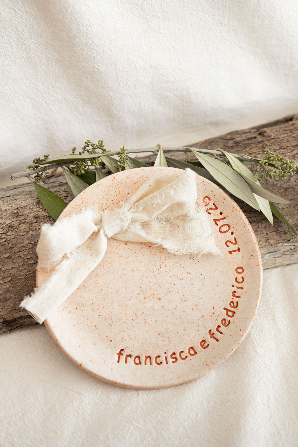 Prato redondo salpicado com fita de tecido cru e folhas verdes sobre madeira.