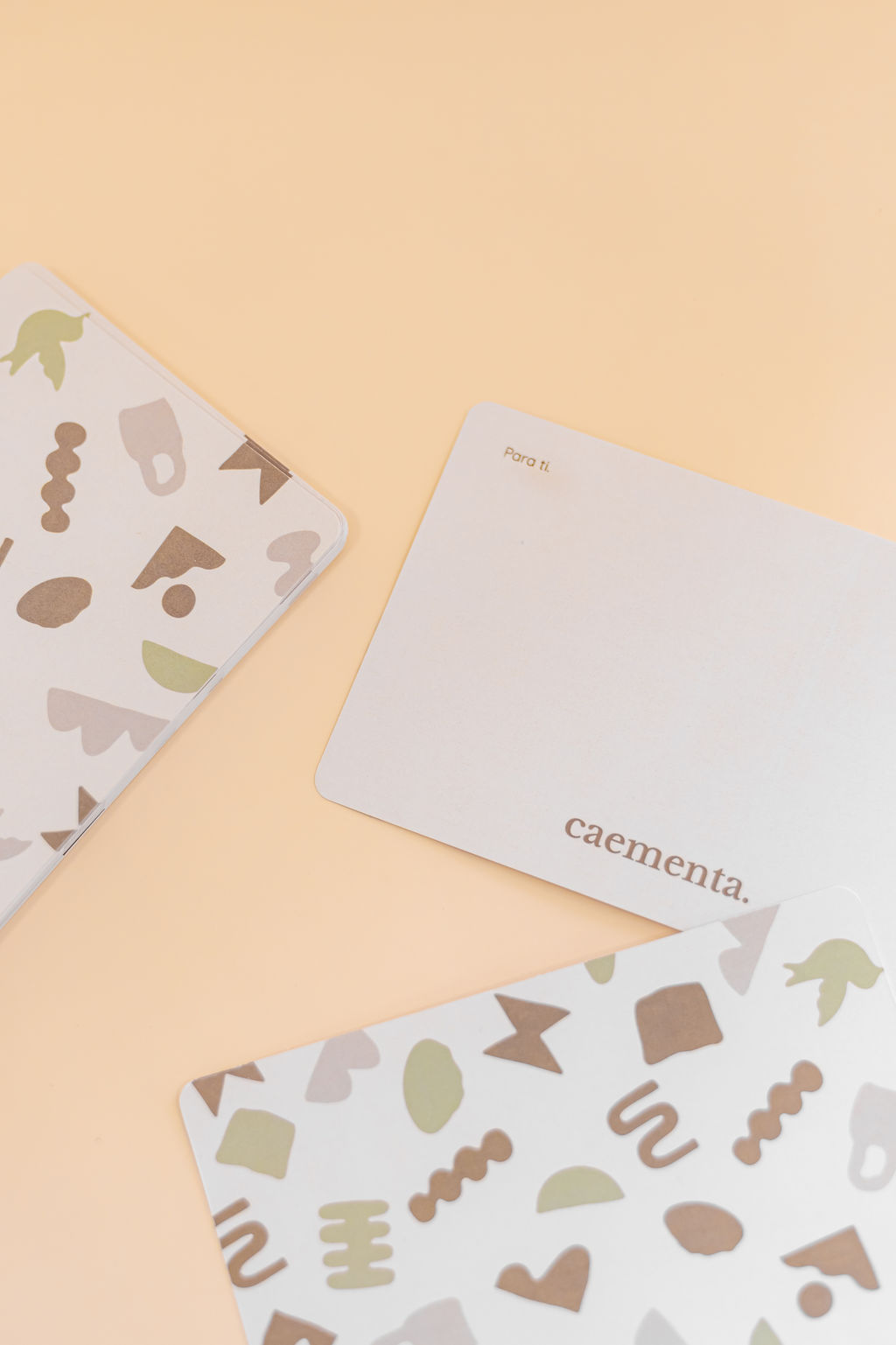Cartões com padrões abstratos em tons terra e cartão branco com texto num fundo bege