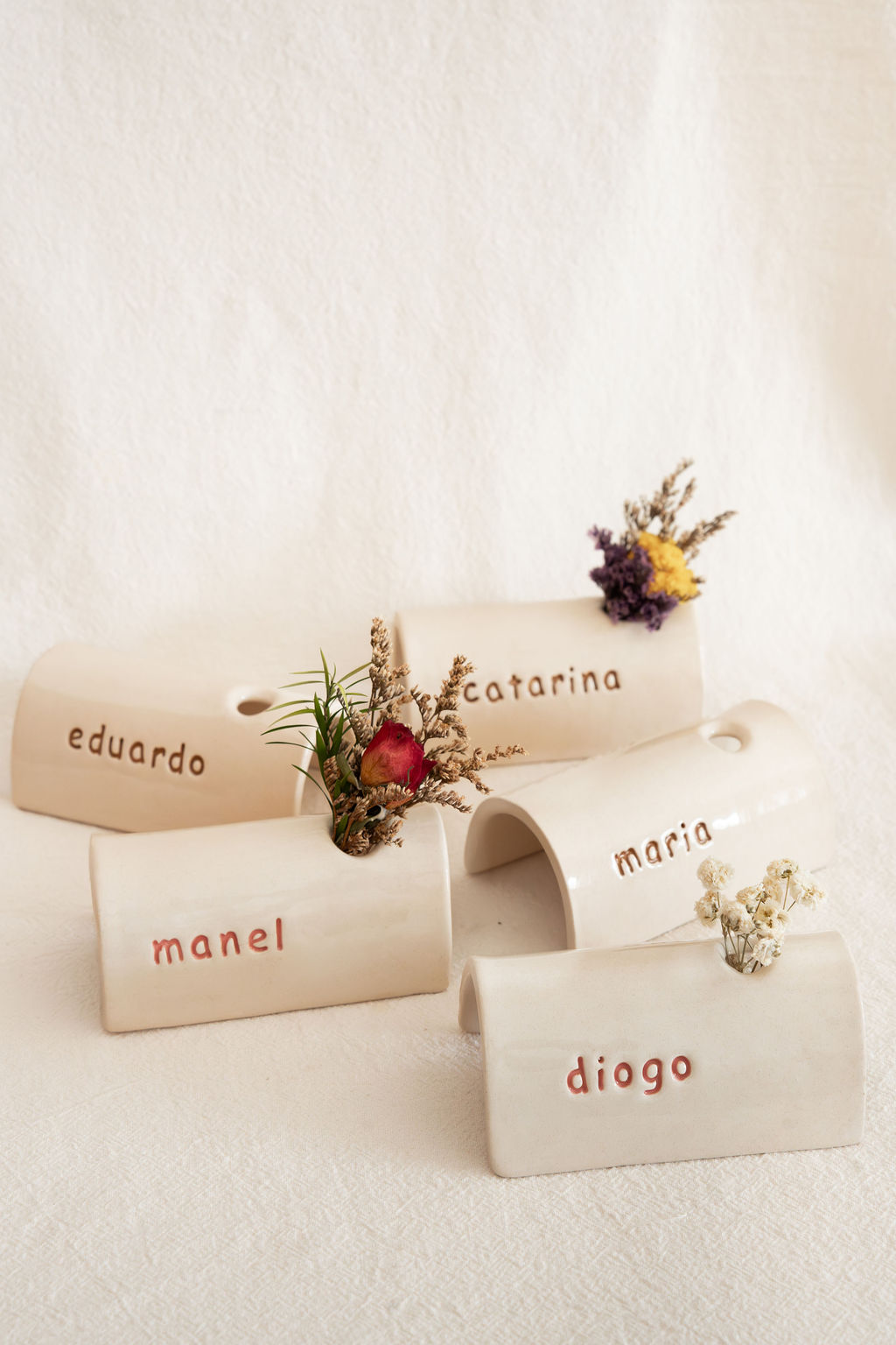 Vasos de cerâmica branca com nomes gravados e flores secas.