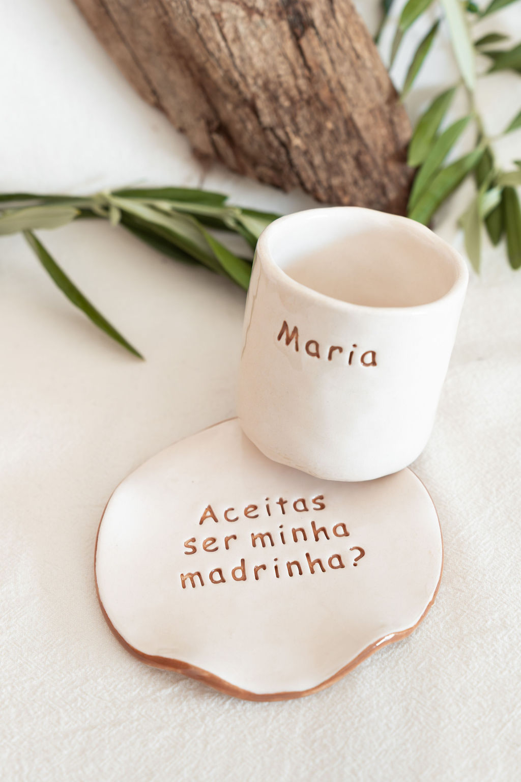 Conjunto cerâmico branco com texto Maria e Aceitas ser minha madrinha? em fundo branco com folhas verdes.