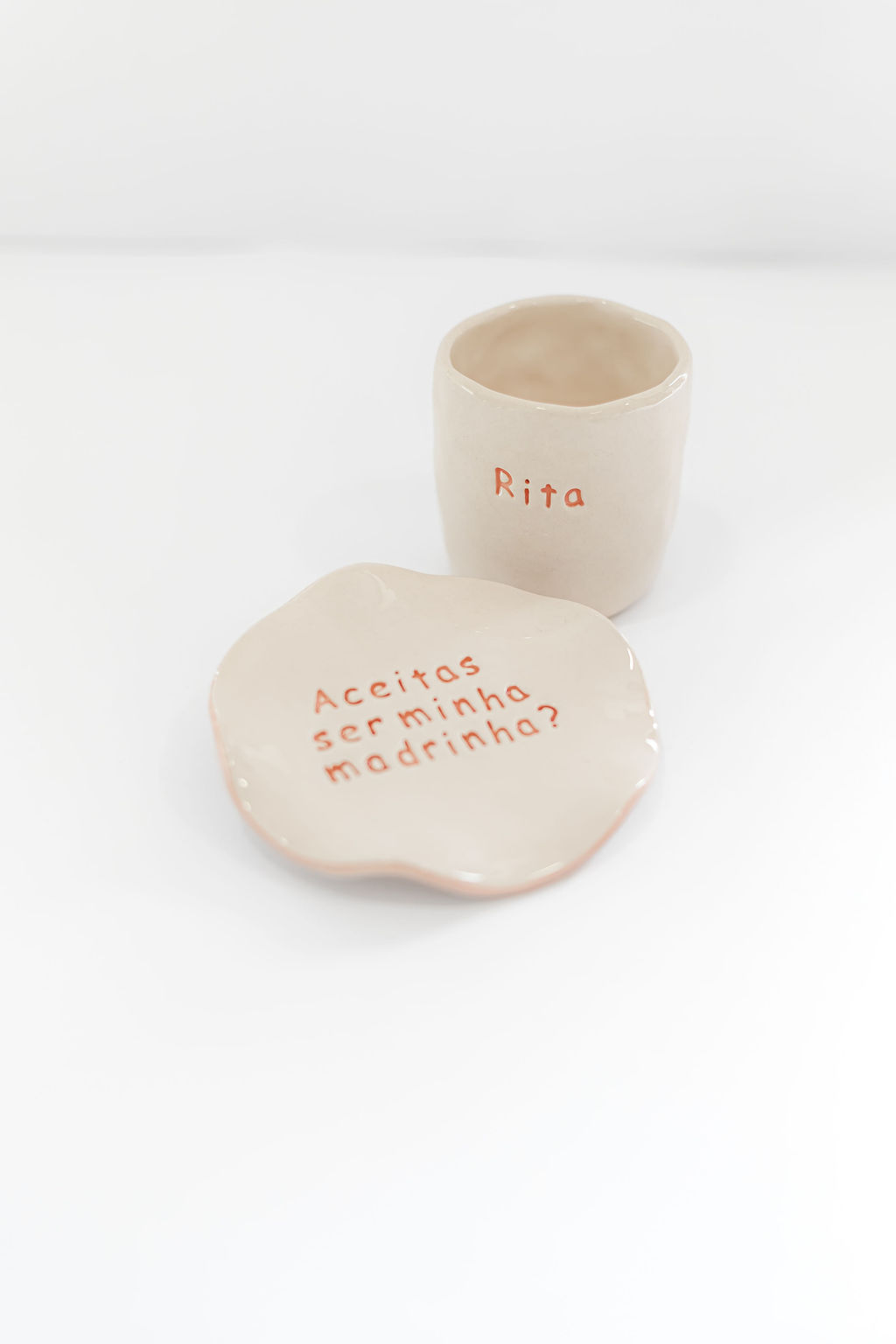 Conjunto cerâmico bege com chávena e prato com texto vermelho
