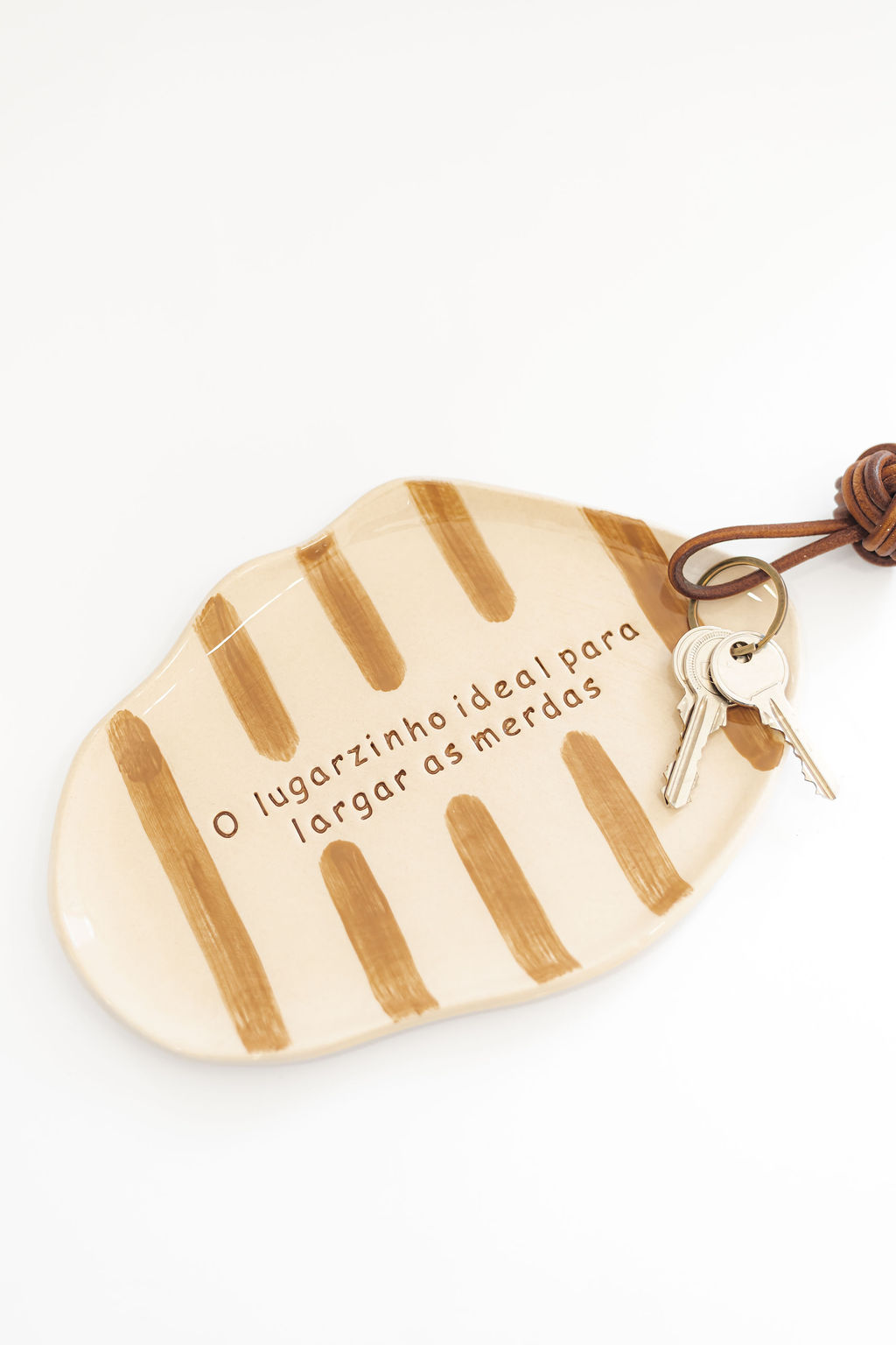 Prato de cerâmica bege com riscas castanhas e texto em português com conjunto de chaves num cordão castanho