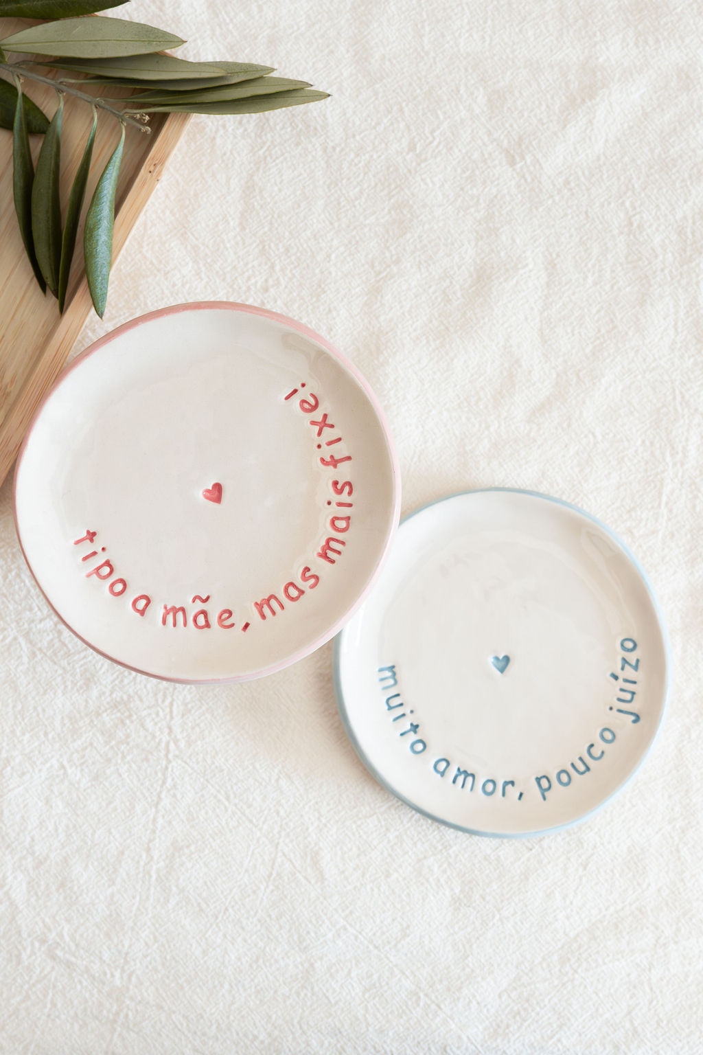 Dois pratos de cerâmica com bordas rosa e azul e texto decorativo em português com corações no centro.