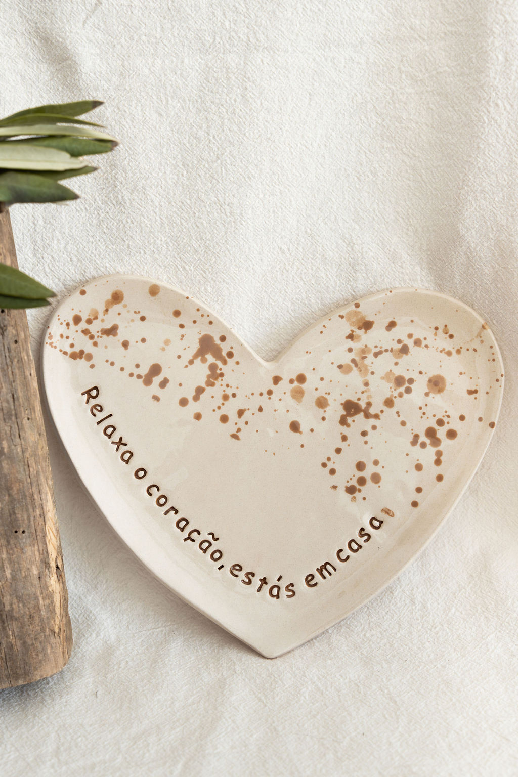 Prato de cerâmica em forma de coração com manchas e frase em português.