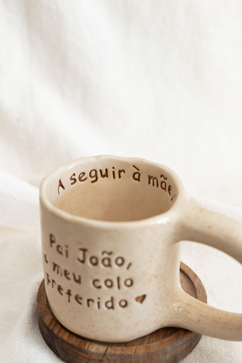 Caneca de cerâmica bege com texto manuscrito castanho e base de madeira