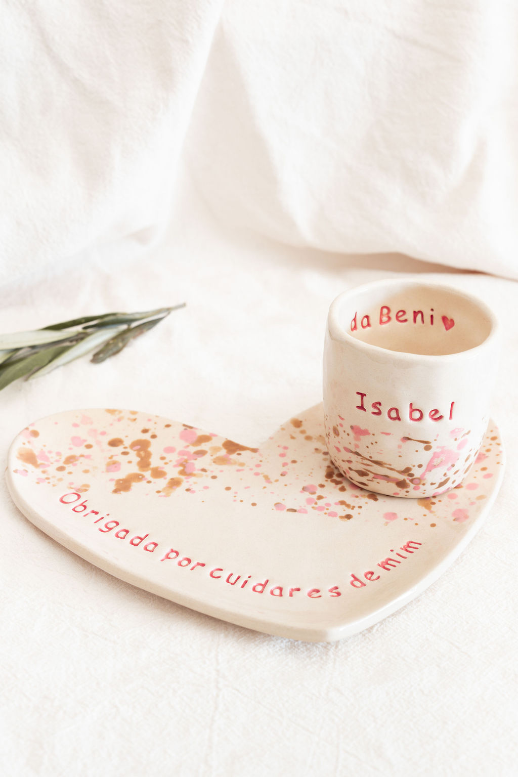 Prato em forma de coração e copo de cerâmica com texto vermelho e manchas coloridas