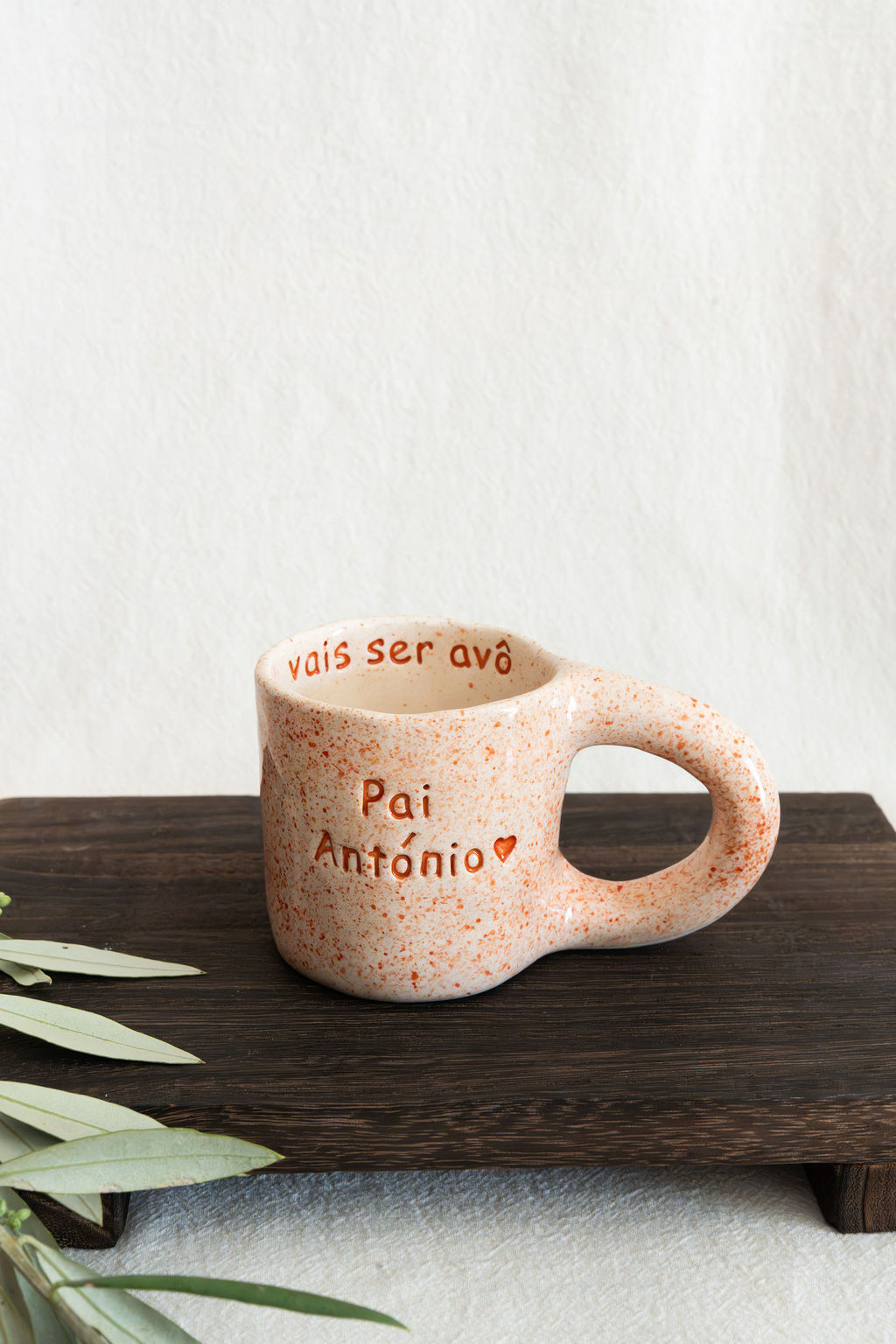 Caneca de cerâmica bege com manchas laranja e texto gravado, em cima de tábua de madeira escura