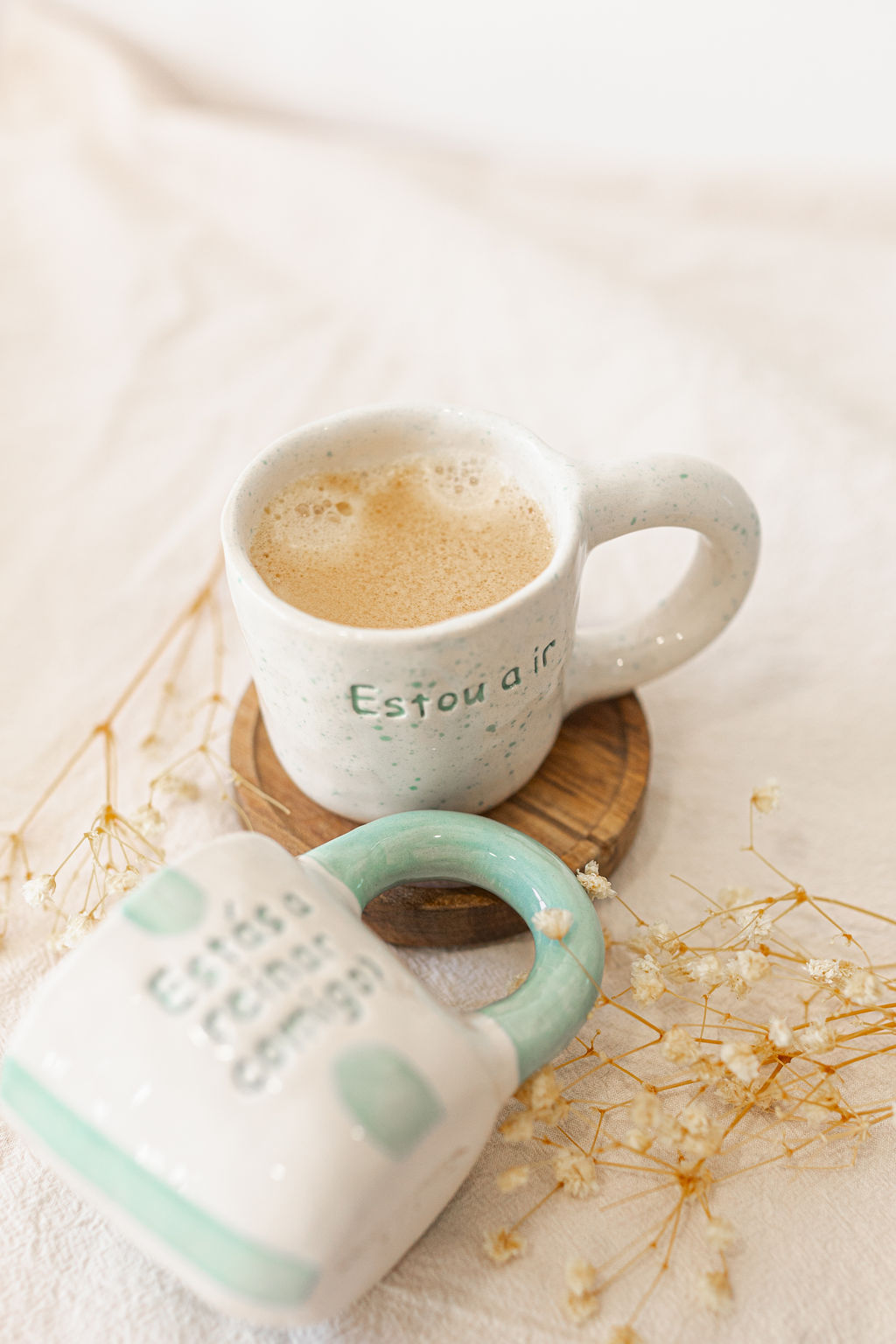 Canecas de cerâmica com textos em português e flores secas numa mesa